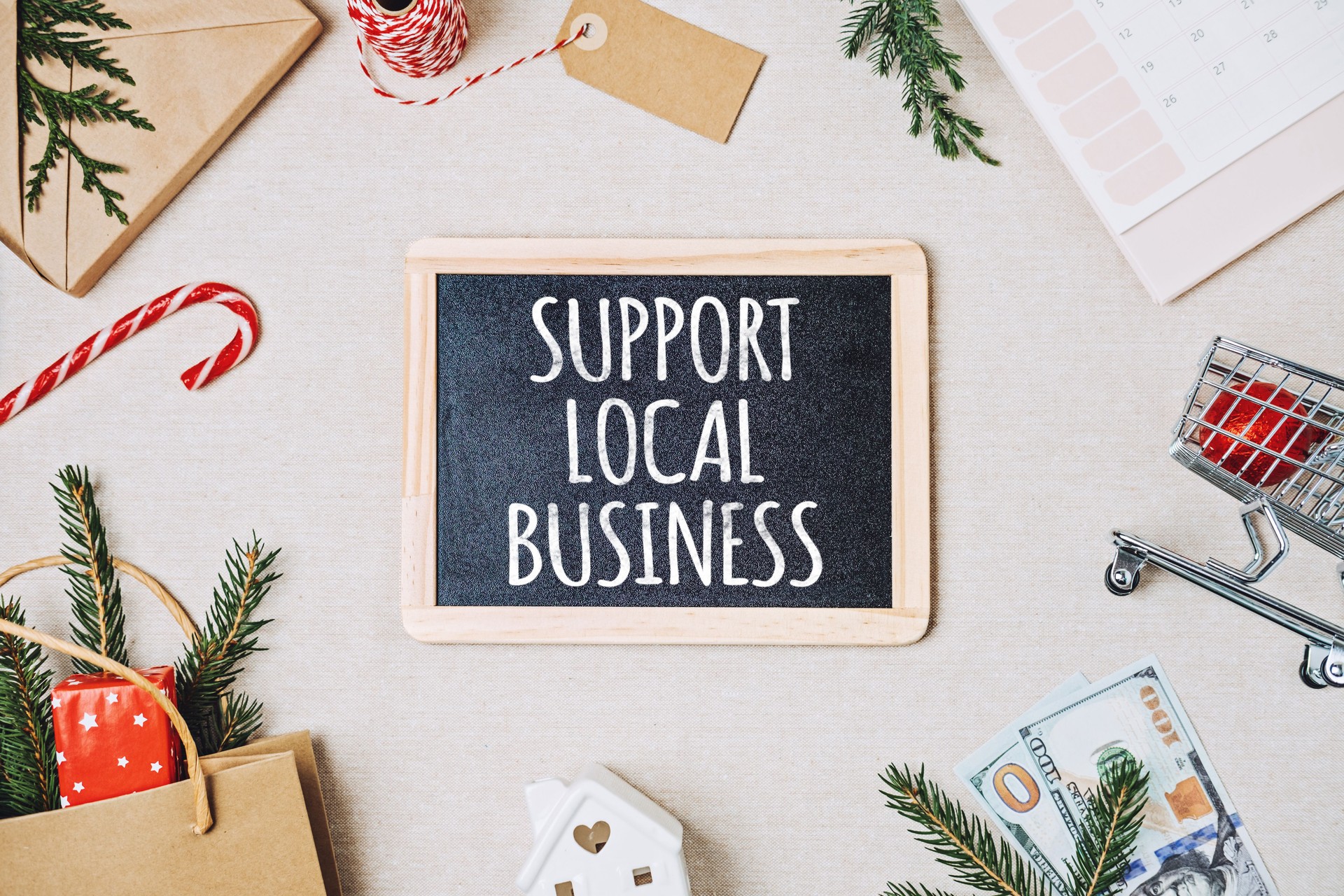 Support Local Business text written on blackboard. Flat lay with Support Local Business quote, Christmas decoration and shopping bag, gift boxes and staff.